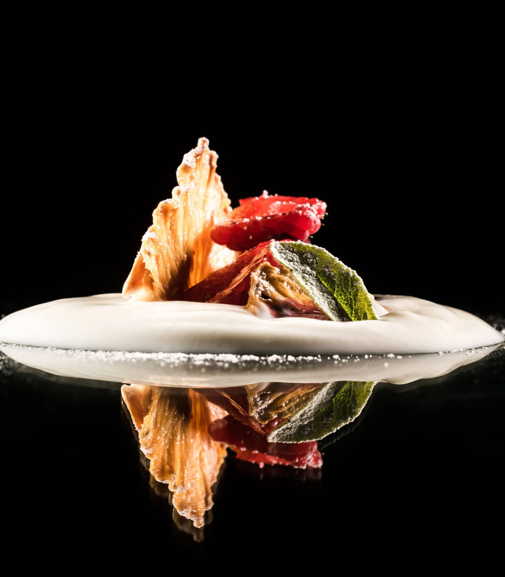 Kreativ angerichtetes Dessert mit Schaum und Fruchtscheiben auf schwarzem Hintergrund