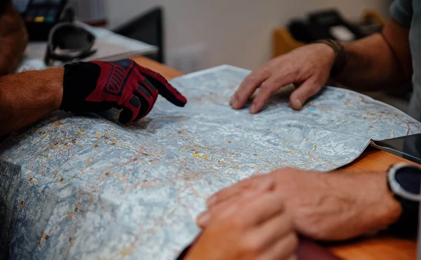 Hahnenkamm Trail © Felix Saller Zwei Personen betrachten und zeigen auf eine Landkarte auf einem Tisch