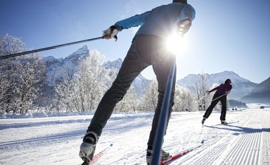 Zwei Personen beim Langlaufen auf verschneiter Strecke vor Bergen