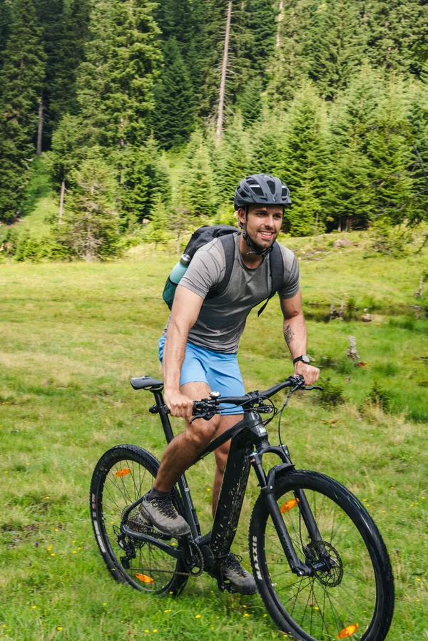 Mann fährt Mountainbike auf einer Wiese mit Wald im Hintergrund