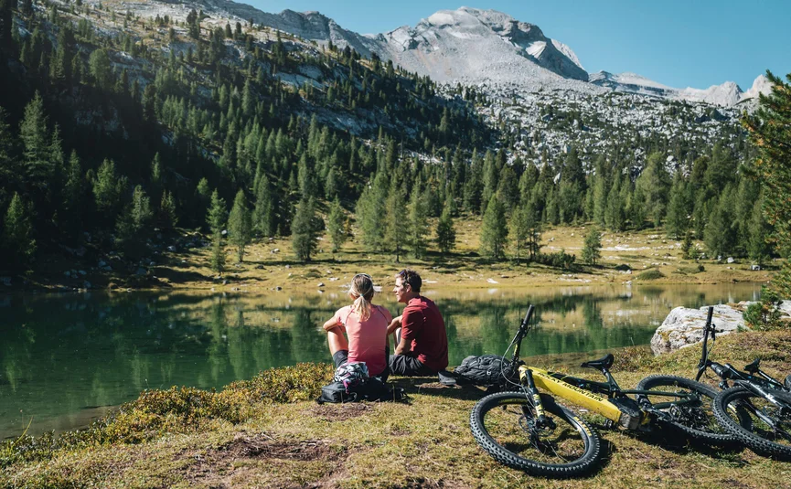 Two cyclists sitting by a mountain lake enjoying the view