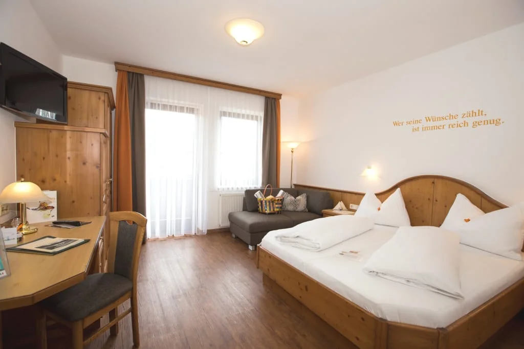 Helles Hotelzimmer mit Bett, Sofa, Schreibtisch und Fernseher