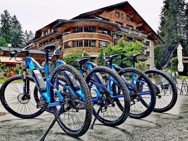 Was steckt hinter dem Umweltengagement von Bikehotels? © Ribno Alpine Resort - Katarina Strgar Vier blaue E-Mountainbikes vor einem Hotel in den Bergen