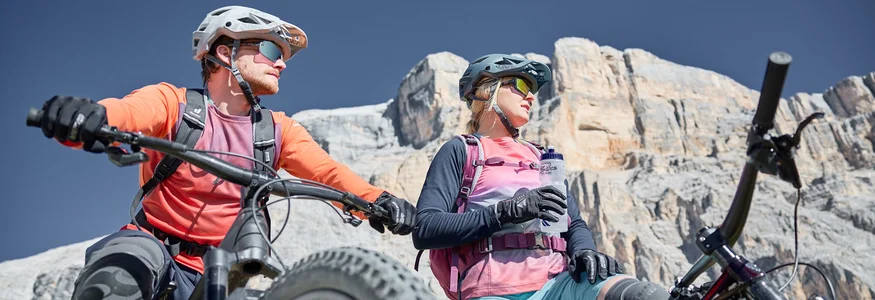 Bikeurlaub per Bahn © Tobias Köhler Zwei Mountainbiker mit Helmen machen Pause vor felsiger Bergkulisse