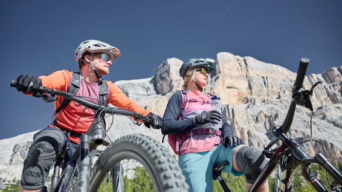 Mountainbike-Urlaub in Alta Badia © Tobias Köhler Zwei Mountainbiker mit Helmen machen Pause vor felsiger Bergkulisse