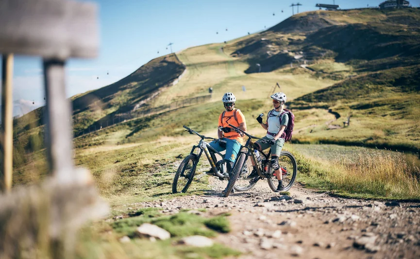Two mountain bikers with helmets resting on a mountain trail in sunny weather