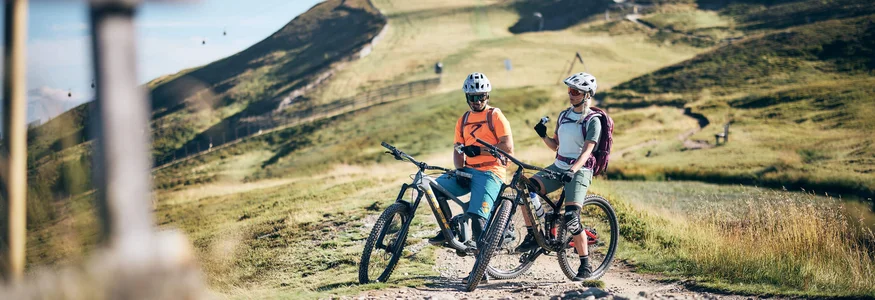 Zwei Mountainbiker mit Helmen pausieren auf einem Bergweg bei sonnigem Wetter