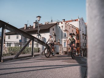 Zwei Radfahrer fahren auf einer Brücke in einer Altstadt bei sonnigem Wetter