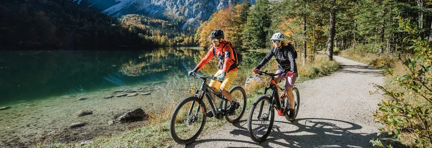 Mountainbikevakantie in Opper-Oostenrijk © Salzkammergut Tourismus - Katrin Kerschbaumer Twee fietsers op bospad naast bergmeer en bergen bij helder weer