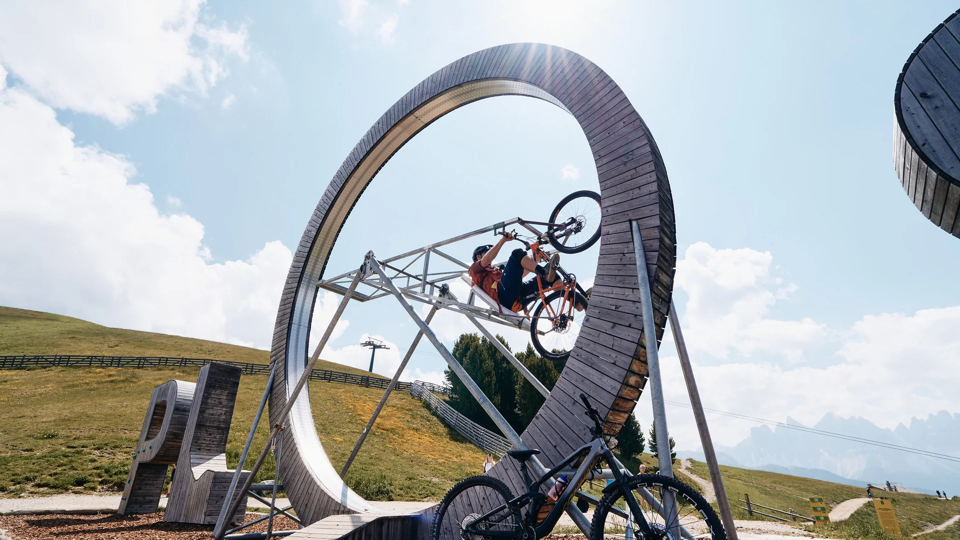 Fahrradfahrer fährt Looping auf Holzrad in Berglandschaft bei Sonnenschein