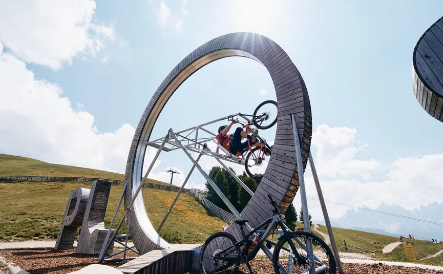 Fahrradfahrer fährt Looping auf Holzrad in Berglandschaft bei Sonnenschein