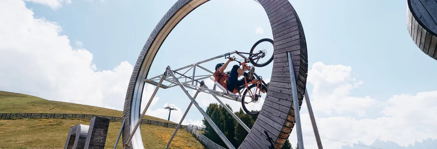Fahrradfahrer fährt Looping auf Holzrad in Berglandschaft bei Sonnenschein