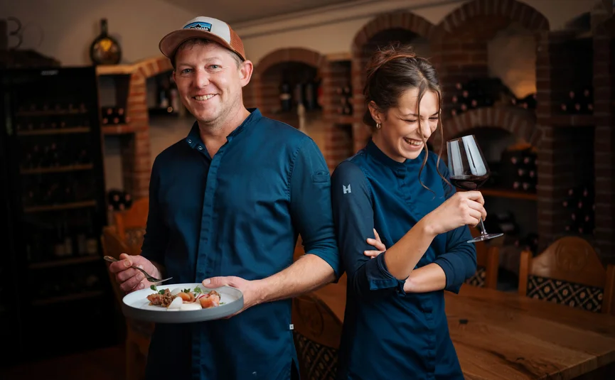 Zwei Köche in blauer Arbeitskleidung in einem Restaurant mit Essen und Glas Wein
