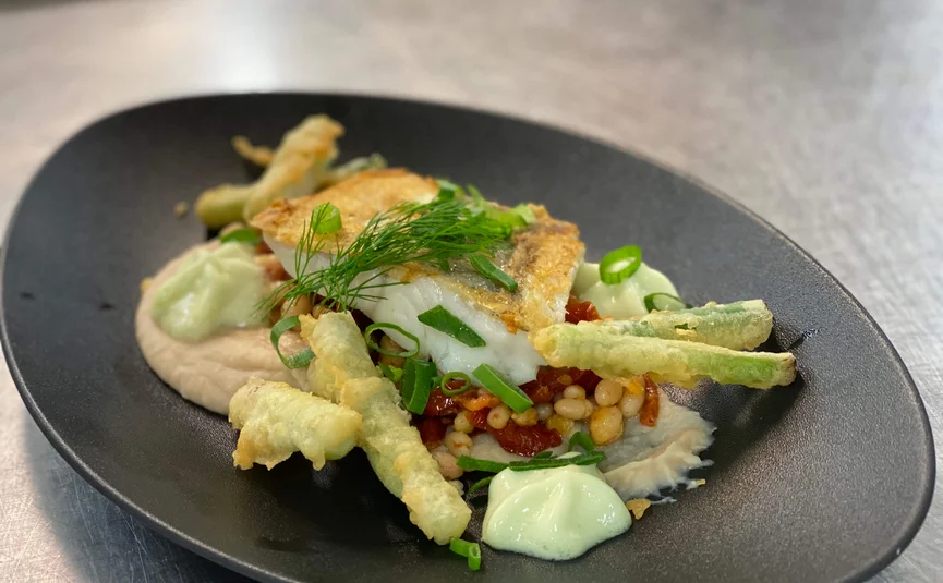 Elegantes Fischgericht mit grünen Bohnen und weißen Bohnen auf schwarzem Teller