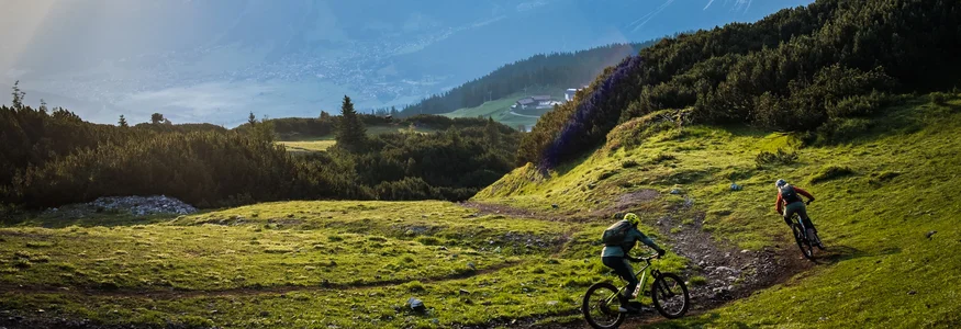 Zwei Mountainbiker fahren auf einem Bergweg bei Sonnenaufgang