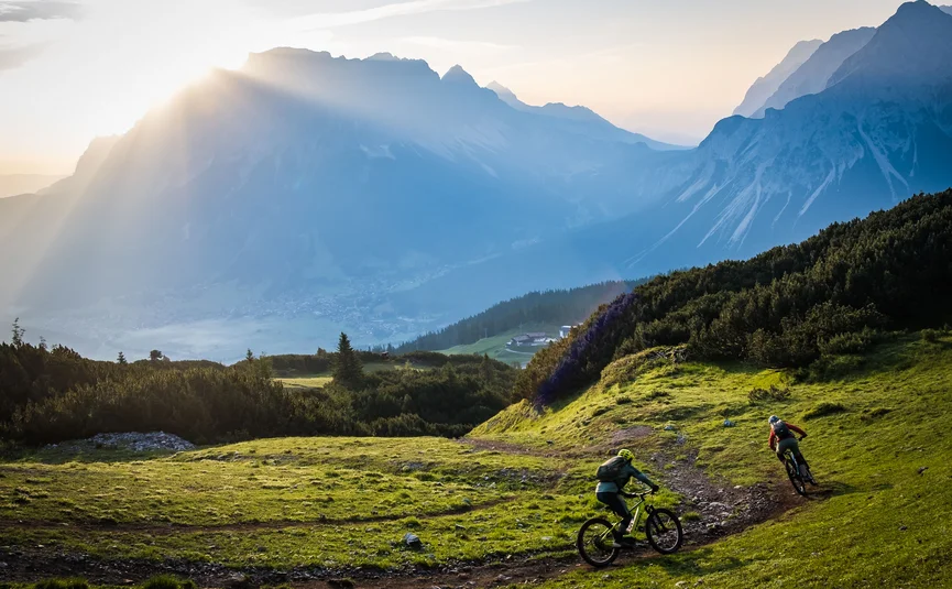 Zwei Mountainbiker fahren auf einem Bergweg bei Sonnenaufgang