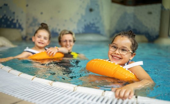 Kind mit Schwimmflügeln lernt schwimmen im Hallenbad mit Erwachsenem
