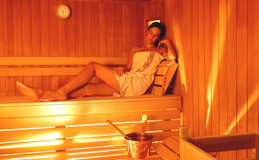 Frau entspannt in Sauna auf Holzbank mit Holzeimer und Kelle