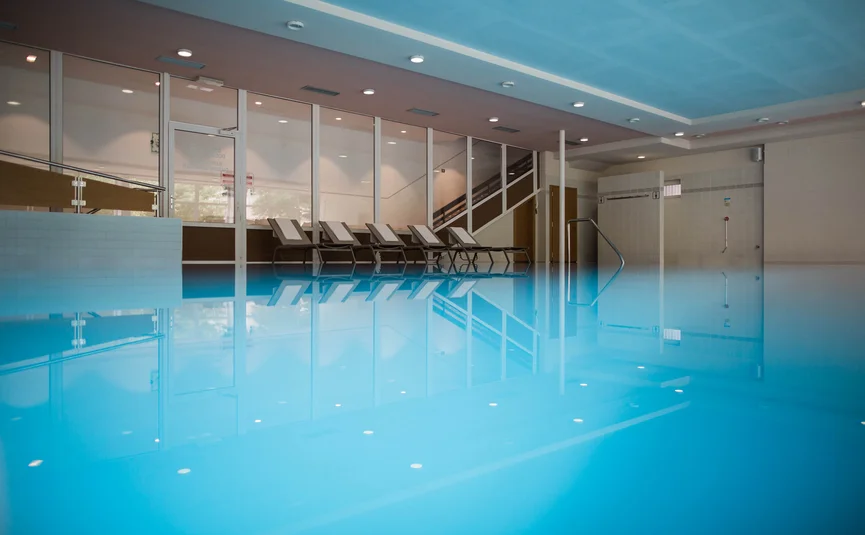 Innenaufnahme eines leeren Hallenbads mit Liegestühlen an der Wand