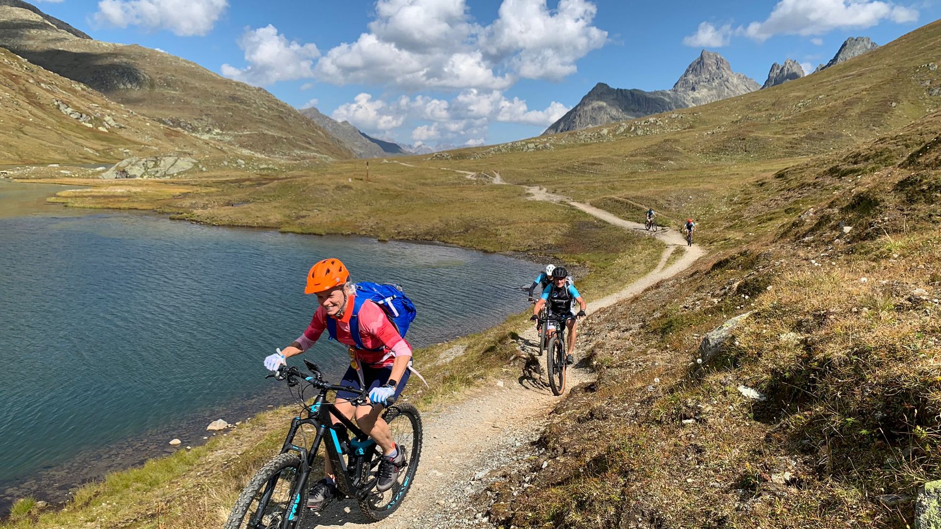 Mountainbiker fahren auf einem Bergweg neben einem See bei klarem Himmel