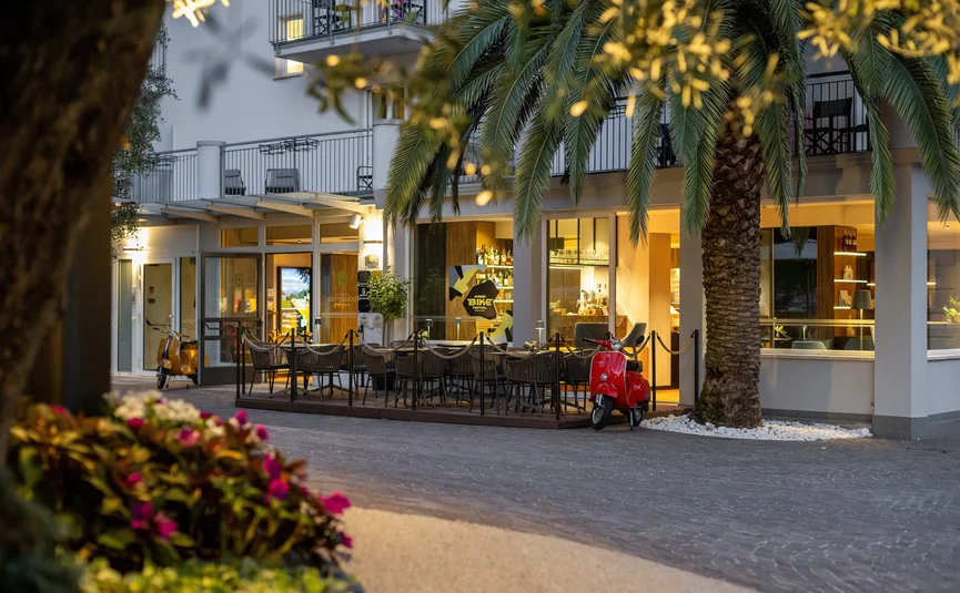 Evening café terrace with red and yellow scooters near palm trees