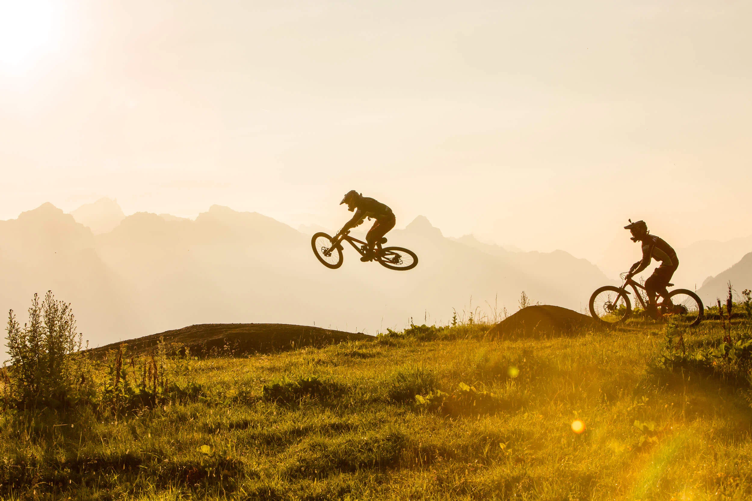 Best of Brandnertal © Michael Marte Zwei Mountainbiker beim Springen in bergiger Landschaft bei Sonnenuntergang