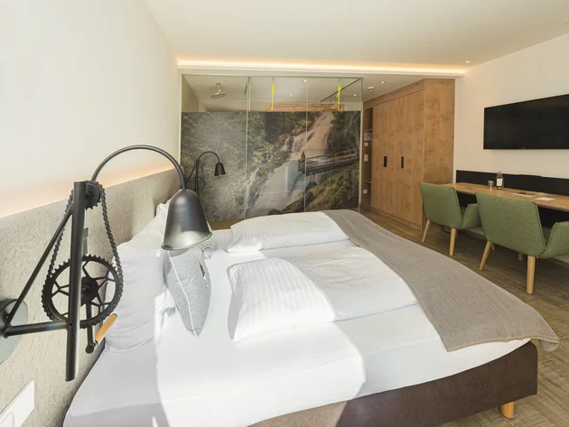 Mit Martina & Flo zum Mountainbiken im LifeSport Hotel Hechenmoos © Martin Raffeiner Modernes Hotelzimmer mit Doppelbett, Fernseher und Naturbild an der Glasdusche