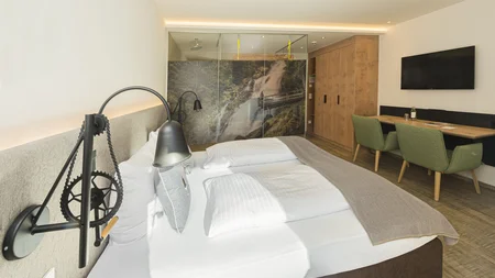 Mit Martina & Flo zum Mountainbiken im LifeSport Hotel Hechenmoos © Martin Raffeiner Modernes Hotelzimmer mit Doppelbett, Fernseher und Naturbild an der Glasdusche