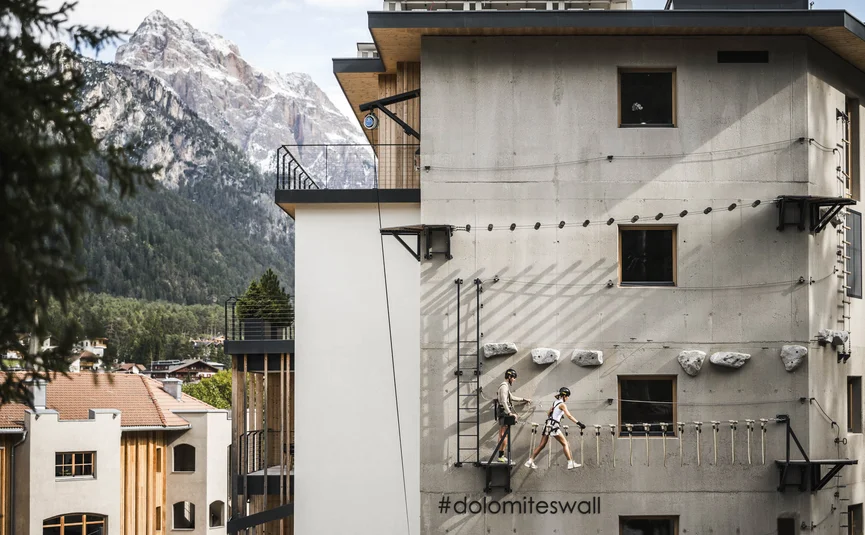 Two climbers on a wall attached to a building with mountain view