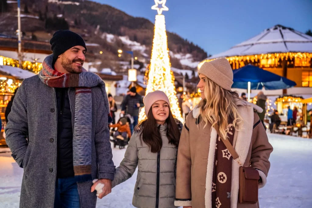 Familie spaziert bei Wintermarkt mit beleuchtetem Weihnachtsbaum