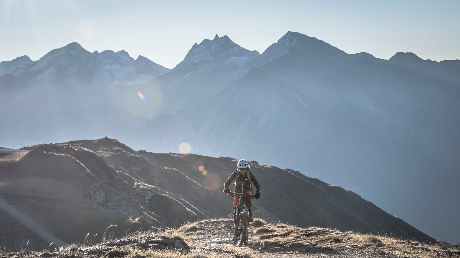 Mountainbiker fährt bergauf vor Alpenkulisse im Sonnenlicht