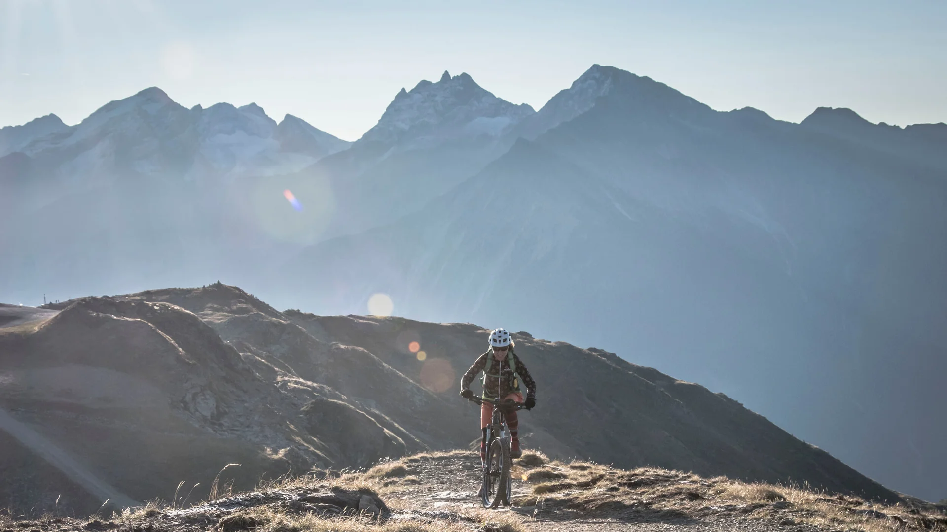 Auf Trail-Mission im Ahrntal © Hipproductions Mountainbiker fährt bergauf vor Alpenkulisse im Sonnenlicht