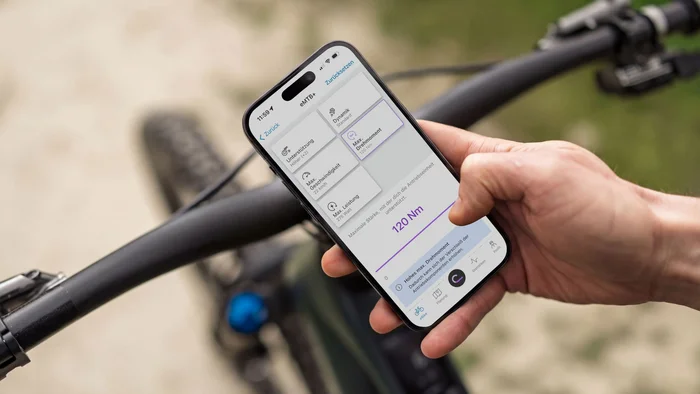 #Uphillflow – der Spaß beginnt schon bergauf © Bosch eBike Systems Hand hält ein Smartphone mit Fahrrad-Einstellungs-App neben einem Fahrrad