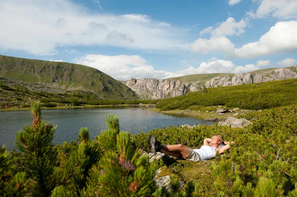 Frau liegt entspannt am See umgeben von Bergen und grüner Landschaft