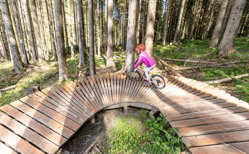 Kind fährt mit Fahrrad auf hölzernem BMX-Rundkurs im Wald