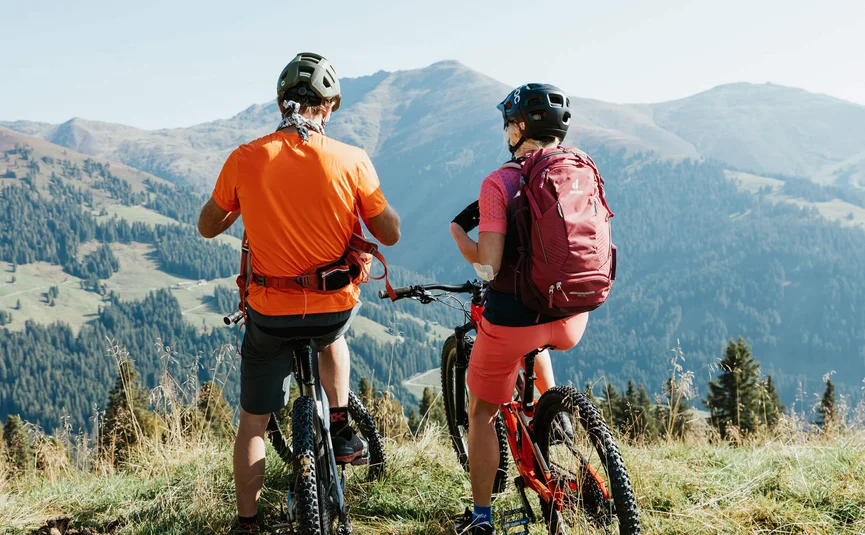 Zwei Radfahrer mit Helm blicken auf Berge und Wald in der Ferne