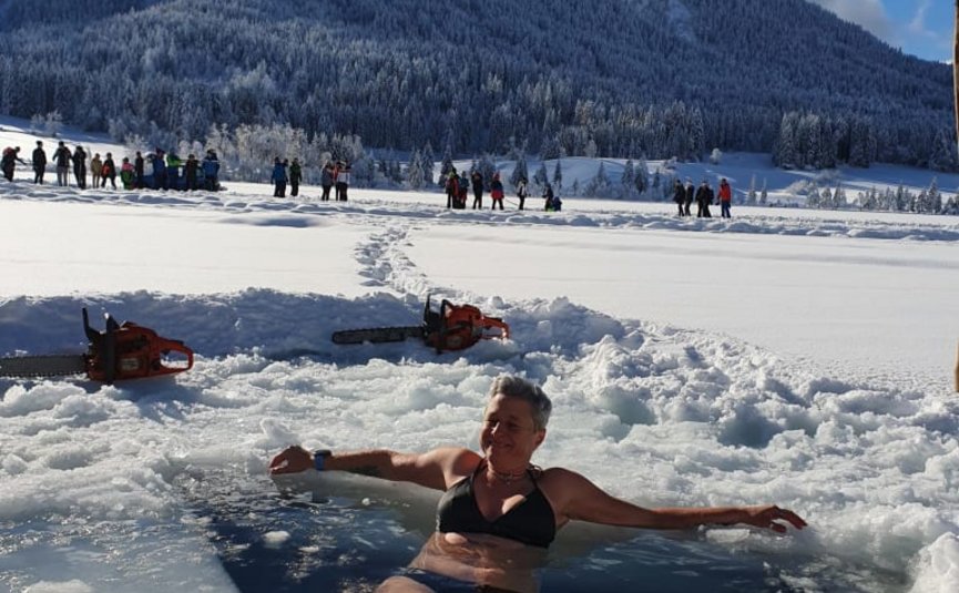 Vrouw in bikini die ontspant in ijsgat met besneeuwde berg en toeschouwers