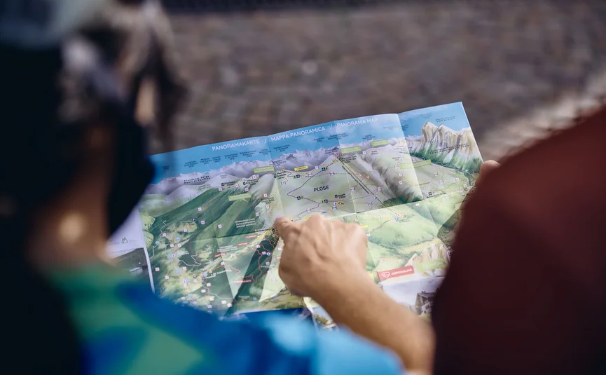 Person zeigt auf eine Panoramakarte von Bergwanderwegen