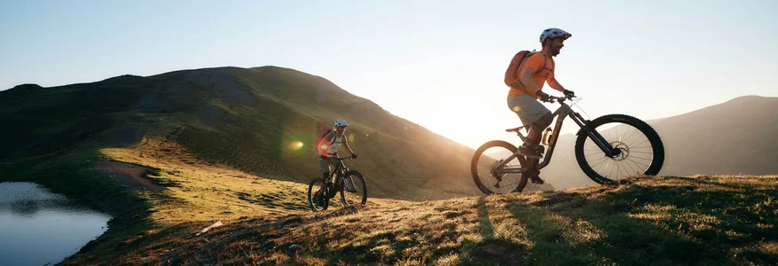 Two mountain bikers cycling on a mountain trail at sunset