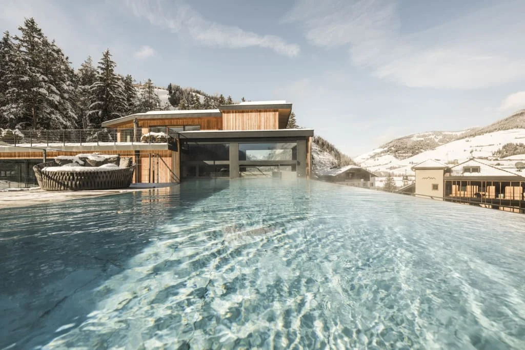 Infinity pool overlooking snow-covered mountains and modern wooden houses