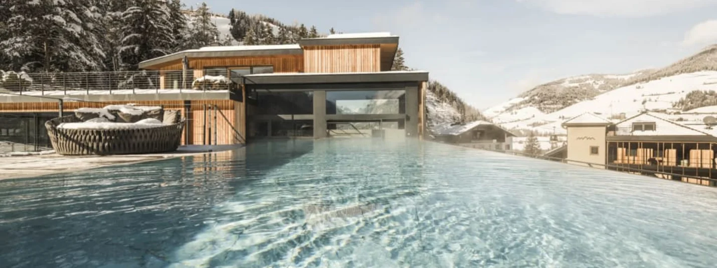 Infinity pool overlooking snow-covered mountains and modern wooden houses