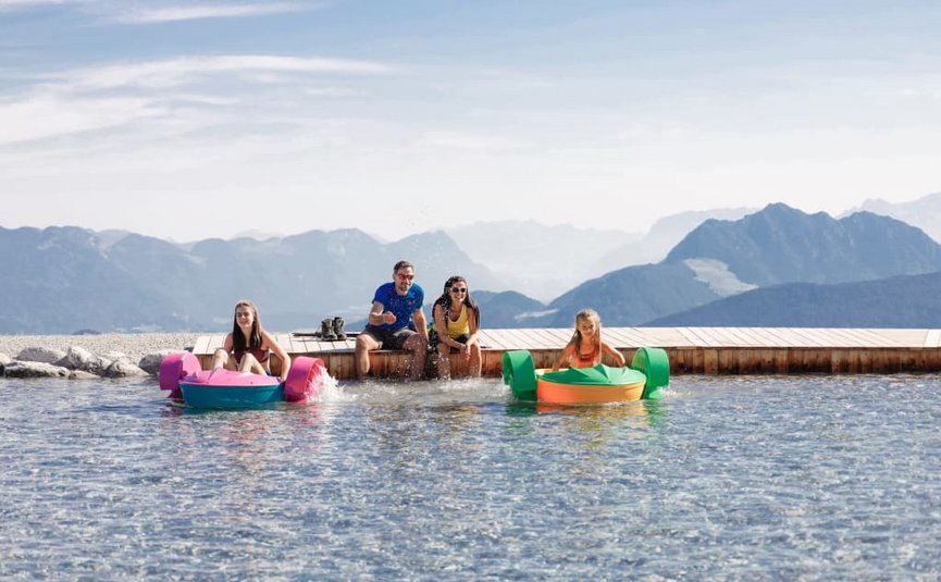 Family playing with children's boats at a mountain lake with mountains in background