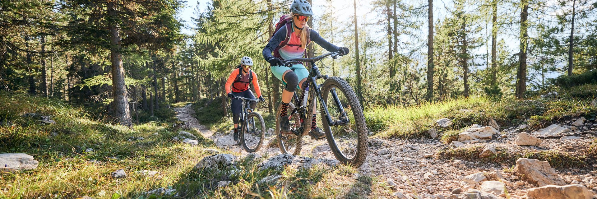 Twee mountainbikers fietsen bergop op een zonnig bospad