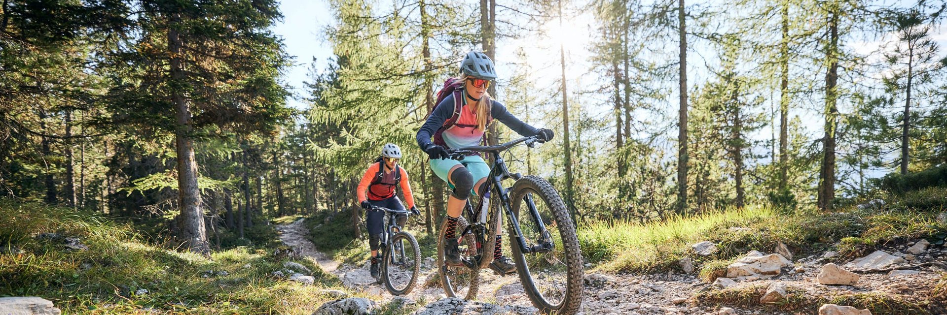 Hotel Pider ***S © Tobias Köhler Zwei Mountainbiker fahren auf einem sonnigen Waldweg bergauf