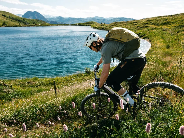 Mit Martina & Flo zum Mountainbiken im LifeSport Hotel Hechenmoos © Martina Wunderle / Flo Distl Mountainbiker mit Helm fährt an einem See in bergiger Landschaft vorbei