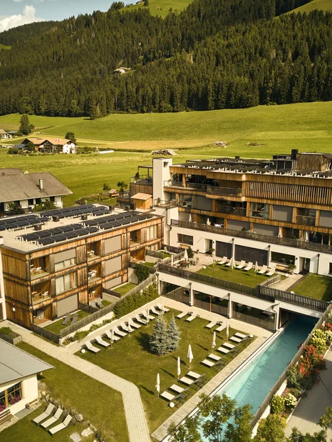 Hotelanlage mit Schwimmbad und Liegestühlen in grüner Berglandschaft