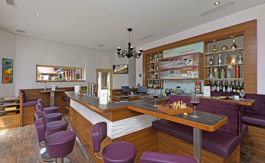 Moderner Barbereich mit lila Sitzhockern und Holztheke mit Schachbrett