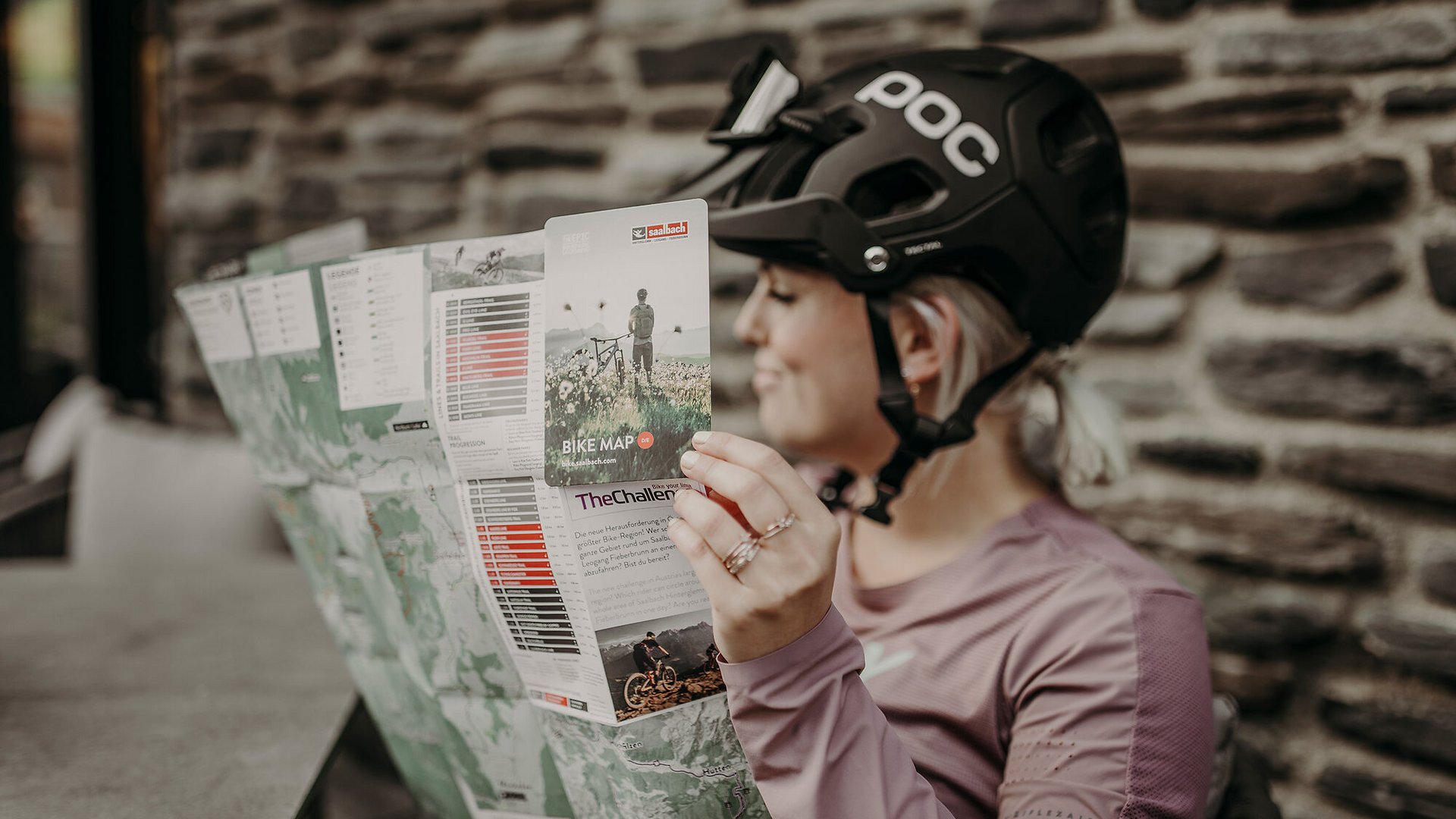 Frau mit Fahrradhelm liest eine Fahrradkarte an einer Steinmauer