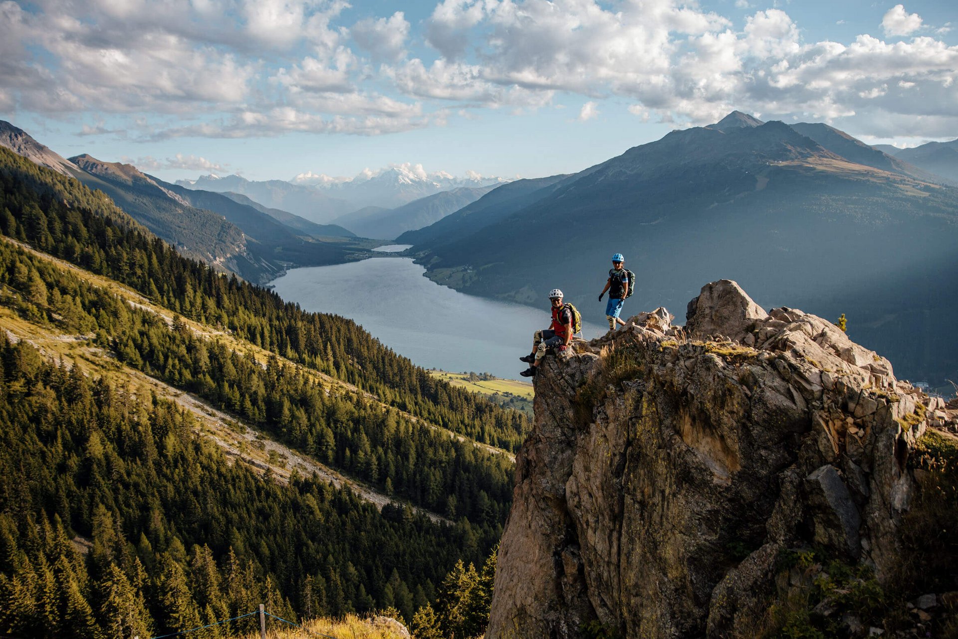 Zwei Wanderer auf Felsen mit Berg- und Seelandschaft im Hintergrund