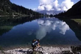 4 Tage Bergsommer rund um die Zugspitze 2026 Fietser aan de oever van het meer met berg- en wolkenreflecties in het water
